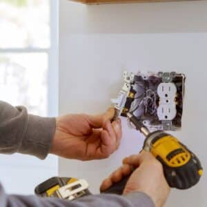foulks electrician holding an electric drill to unscrew a light switch and power outlet