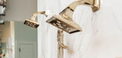 two gold-colored shower heads installed on a marble bathroom wall