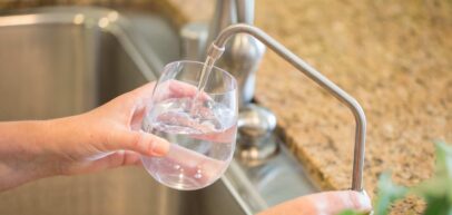 Woman Pouring Fresh Reverse Osmosis Purified Water Into Glass in Kitchen.